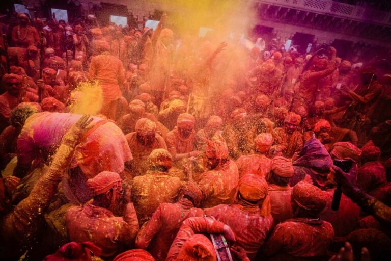 Group of people joyfully throwing vibrant colored powders during Holi celebrations, symbolizing the festival's spirit of unity and love.